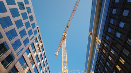A large tower crane in the downtown of the modern city. Glass office buildings around. Low angle...