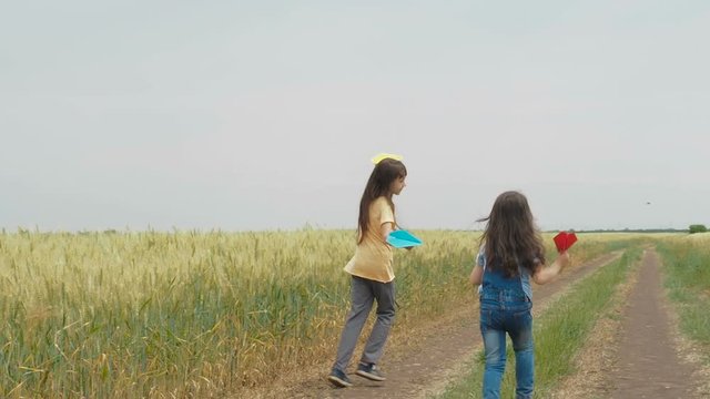 Children play with paper planes. Little girls with paper airplanes in the field.