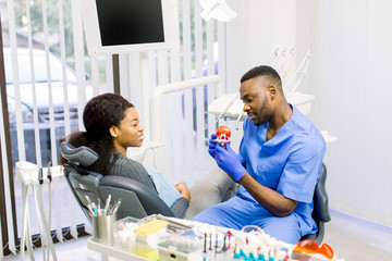 Friendly male dentist showing teeth model to his patient