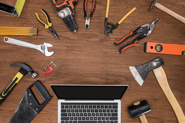 top view of laptop with blank screen surrounded by arranged various tools on wooden table