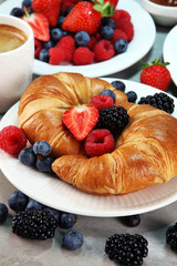Delicious breakfast with fresh croissants and ripe berries on old marble background.