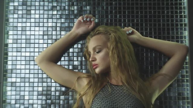 Beautiful sexy blonde girl with wet hair. Posing in a swimsuit in the shower under the drops of water. Slow motion