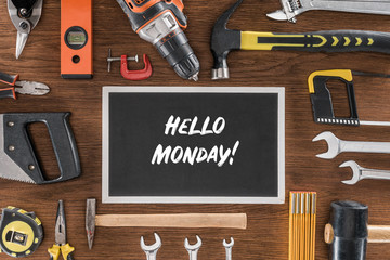 top view of blackboard with lettering hello monday near arranged various tools on wooden table