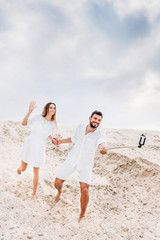 playful young couple taking selfie with monopod and smartphone in desert