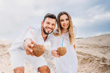 happy young couple in white with coconut cocktails looking at camera