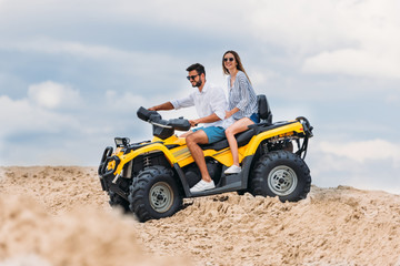 happy young couple riding all-terrain vehicle in desert on cloudy day