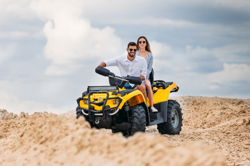 active young couple riding all-terrain vehicle in desert on cloudy day
