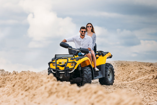 active young couple riding all-terrain vehicle in desert on cloudy day