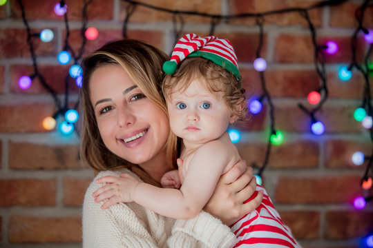Beautiful little baby boy in elf hat and mother with fairy lights on background. Christmas time season image