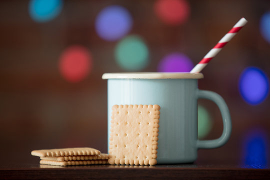 Hot cup of coffee and classic cookie with fairy lights on background. Christmas season