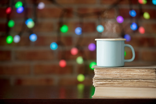 Hot cup of coffee and books with fairy lights on background. Christmas season