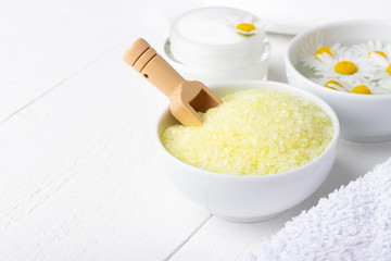 Spa background with bath yellow sea salt, natural cream and chamomile on white wooden table