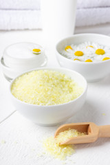 Spa background with bath yellow sea salt, natural cream and chamomile on white wooden table