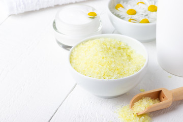 Spa background with bath yellow sea salt, natural cream and chamomile on white wooden table