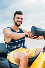 happy young man on all-terrain vehicle looking at camera in front of cloudy sky