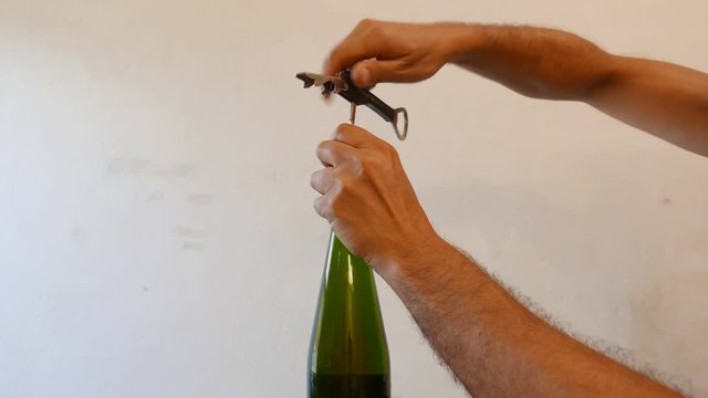 man opening bottle of wine with corkscrew at home