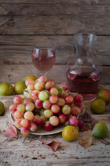 Rose wine with grapes and plums on wood rustic background. 