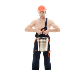 Painter in overalls hold paint bucket. Confident painter, decorator with color bucket. Repair concept. Sexy muscular laborer in protective helmet in overalls. Builder, industrial worker in coveralls.