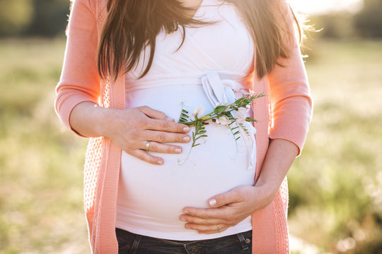 Pregnant mother outdoors on a field resting her hands on her belly