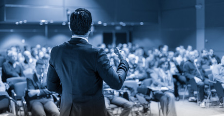 Speaker giving a talk on corporate business conference. Unrecognizable people in audience at conference hall. Business and Entrepreneurship event. Blue toned grayscale image. - obrazy, fototapety, plakaty