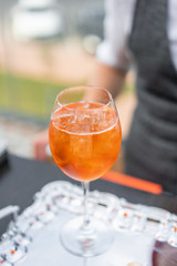 Aperol spritz cocktail in misted glass, selective focus. Alcoholic beverage based on bar counter with ice cubes and oranges. metal shakers in the background