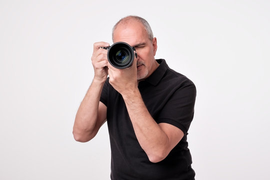 Studio shot of ymature spanish man with camera against grey background. Experienced photographer in photo studio