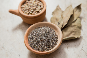 Composition with pottery bowls containing chia seeds, and lentils. Laurel Nobilis leafs. Marble surface.