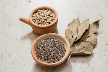 Composition with pottery bowls containing chia seeds, and lentils. Laurel Nobilis leafs. Marble surface.