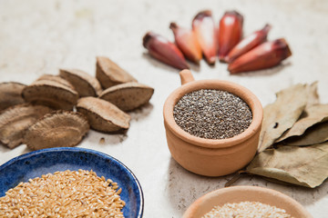 Composition with pottery bowls containing chia seeds, linum seeds, and sesame. Castanha-do-Pará nuts and pinion fruits. Laurel Nobilis leafs. Marble surface.