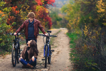 Naklejka premium curly-haired mustachioed guy and an ore-haired girl in autumn stand with bicycles on road and show cheerful emotions.