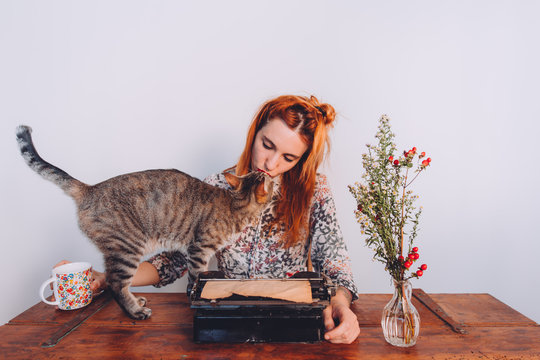 woman trying to work while her cat is playing whit the typewriter