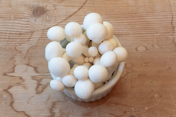 Small dish of white mushrooms centered on an old wood tabletop, horizontal aspect