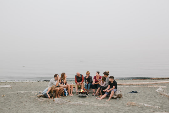 Multi generational family hanging out together around fire on the beach