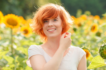 young girl enjoying nature on the field of sunflowers at sunset, portrait of the beautiful redheaded woman girl with a sunflowers in a sunny summer evening