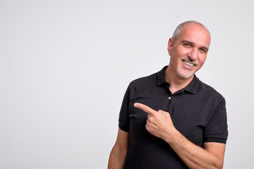 Mature hispanic man pointing aside copy space. Handsome elder man in black shirt looking at camera...