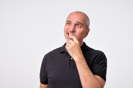 Mature hispanic man thinking with hands on chin looking away. Close up portrait of real people. Concept photo of puzzled, confused, worried and thoughtful man
