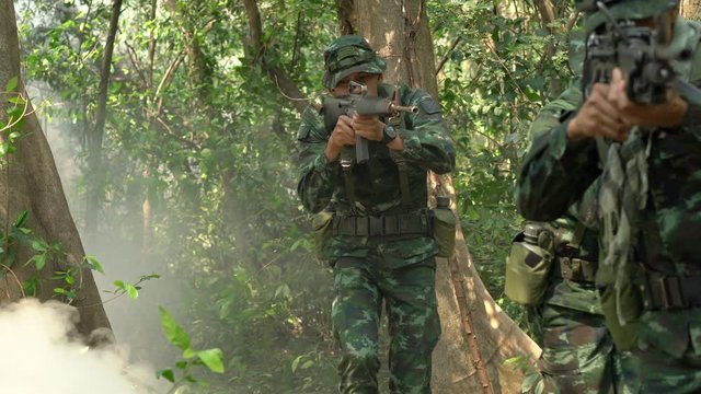 Soldier holding gun weapon and waring armor uniform with smoke camouflage in forest. The military is responsible for maintaining the territory.