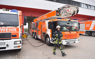 Fototapeta premium Portrait of a young friendly fireman in front of a fire station and fire engine - rescue service