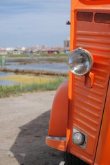 Parte da frente de carrinha antiga cor de laranja com chapa canelada parada ao ar livre num...