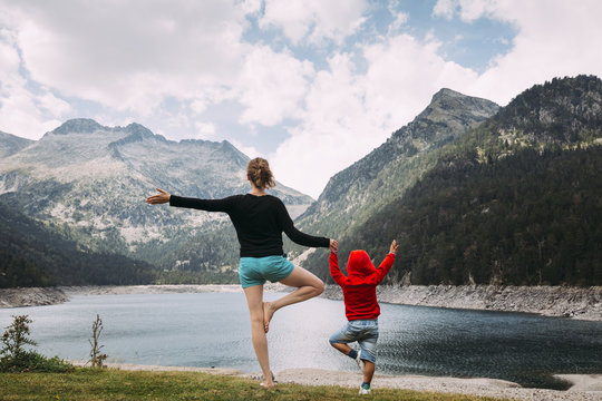 Young woman and her little boy doing yoga in front of a lake in the mountains