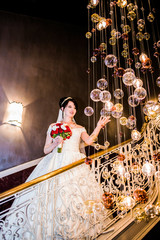 The charming bride is standing in the hotel's lobby near the chandelier