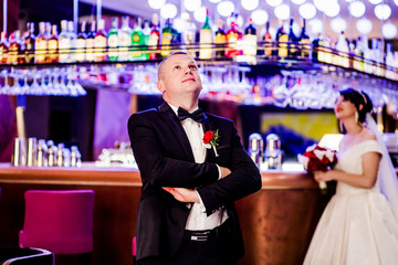 Elegant groom in the restaurant room. Bride in the background