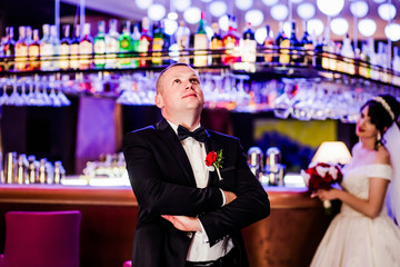 Beautiful groom in the restaurant room. Bride in the background