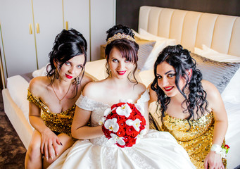 Sweet bride and girlfriends are sitting on the bed