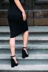 Beautiful girl's legs in a black dress, standing on the stairs
