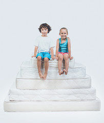 Girl and Boy Sitting on Top of Pyramid of Mattress