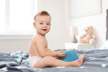 Adorable little baby with book on bed at home