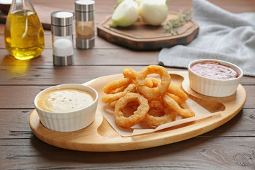 Plate with fried onion rings and sauces on table