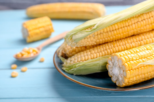 Plate with tasty sweet corn cobs on wooden table, closeup