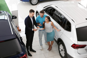 Salesman consulting young couple in car salon